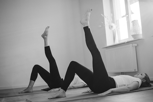 Zwei Pilates Teilnehmerinnen liegen auf dem Rücken und strecken ein Bein gerade nach oben