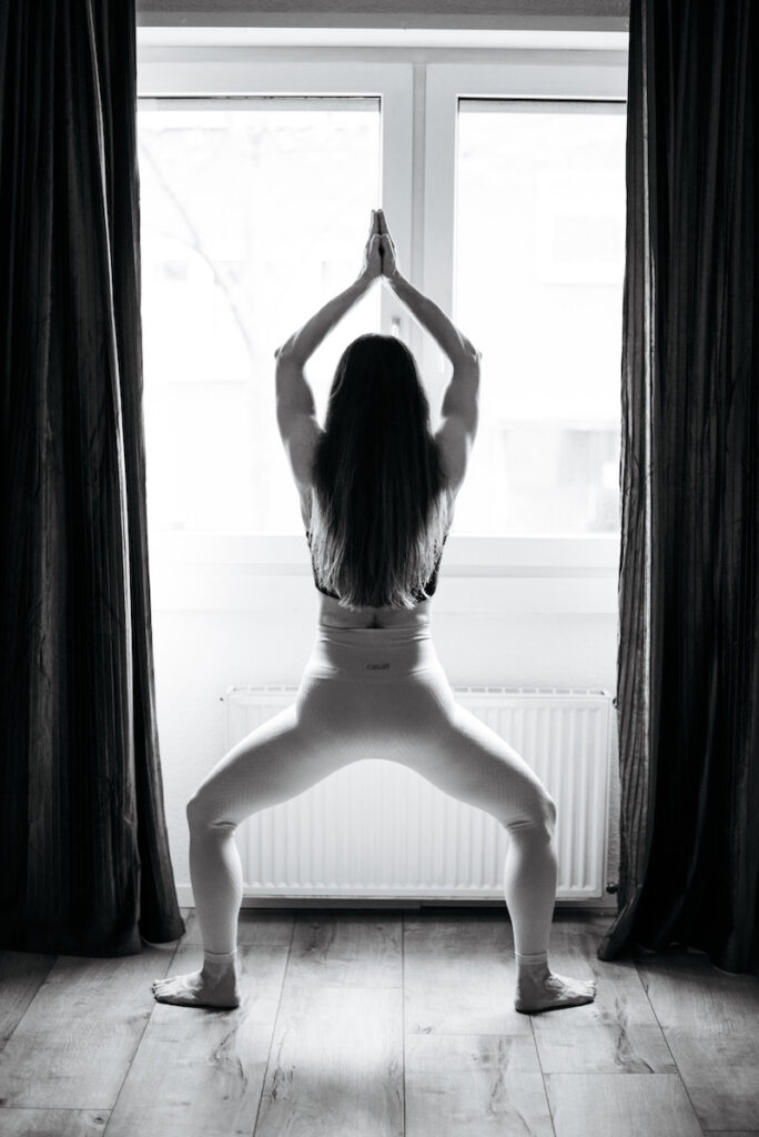 Maria in einer Yoga Pose stehend vor dem Fenster
